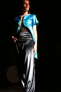 Model wears a blue satin overshirt with black slinky pants.